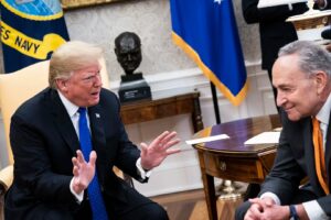 Sen. Chuck Schumer in the Oval Office with President Donald Trump. Schumer is smiling blandly as President Trump scowls.