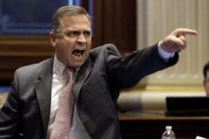 A furious man in a suit, pointing and shouting.