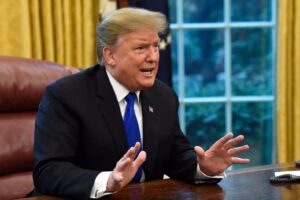 Trump sitting at the Resolute desk, hands spread, mouth open, clearly angry.